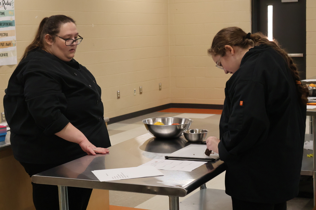 A student is standing with her teacher learning how to cut chocolate as a garnish. 