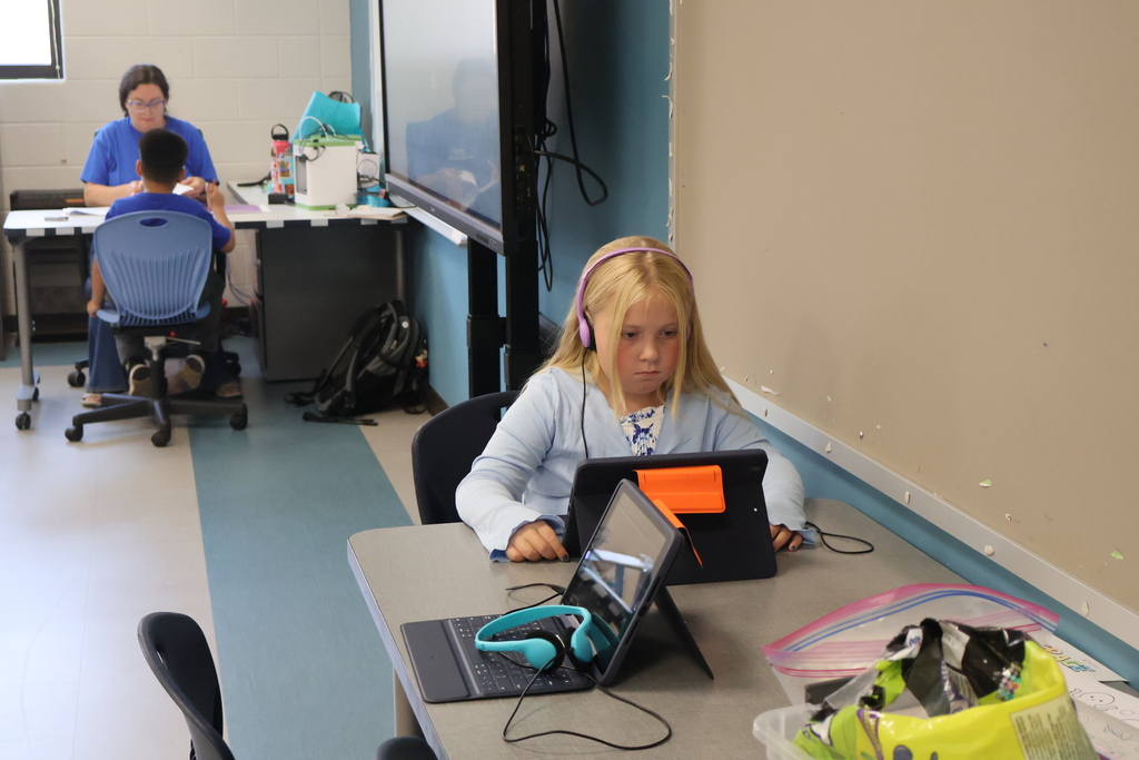 A student is sitting at a table wearing headphones while also working on a computer. 