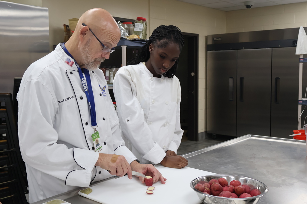 The teacher is showing a student the proper way to cut up purple potatoes. 