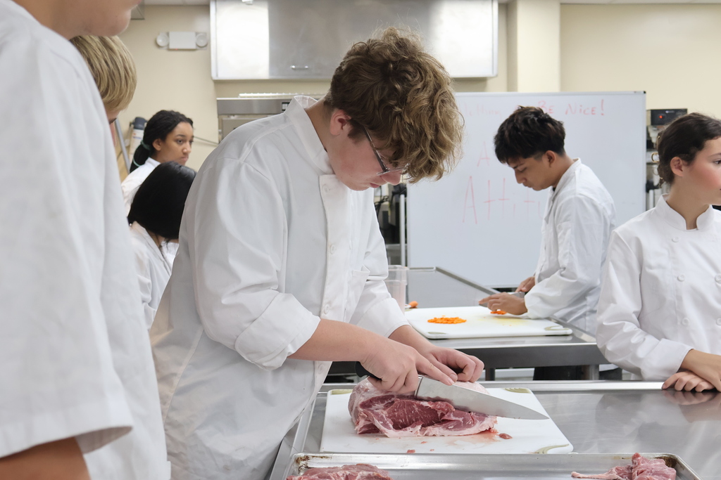 A student is cutting up pieces of pork. 