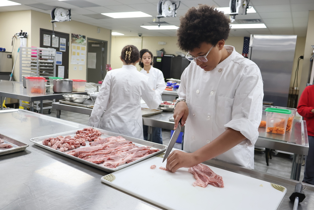 A student is cutting up pieces of pork. 