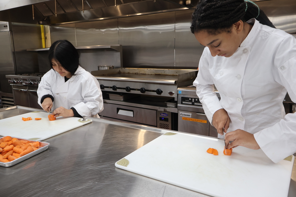 Two students are cutting up carrots. 