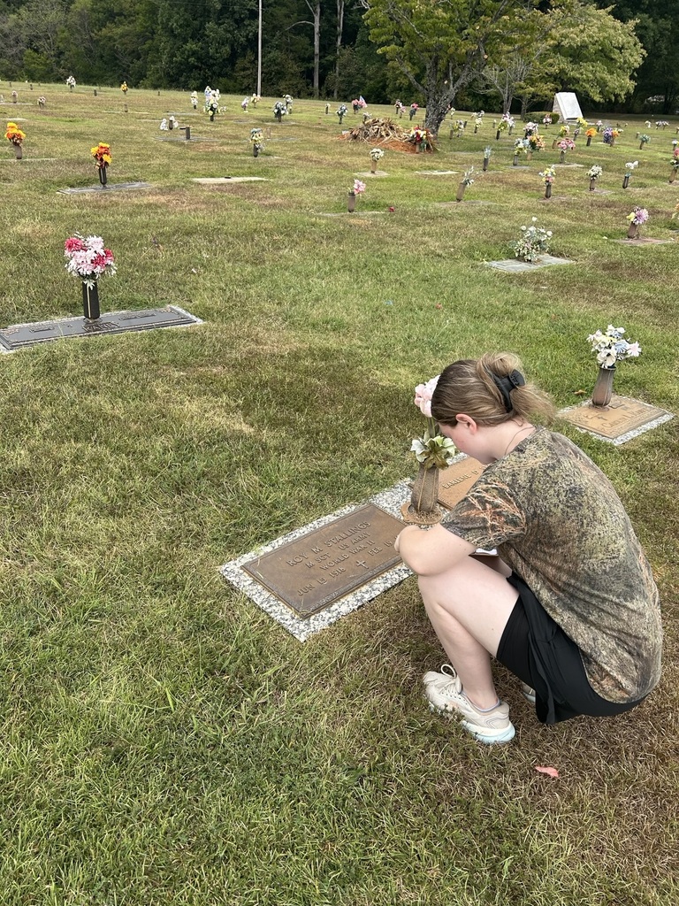 A students is writing down information about the service member at the cemetery. 