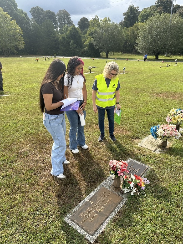 There are two students and a teacher discussing the service members information at the cemetery. 