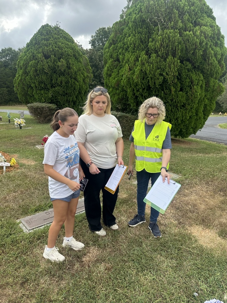 There are two students and a teacher discussing the service members information at the cemetery. 