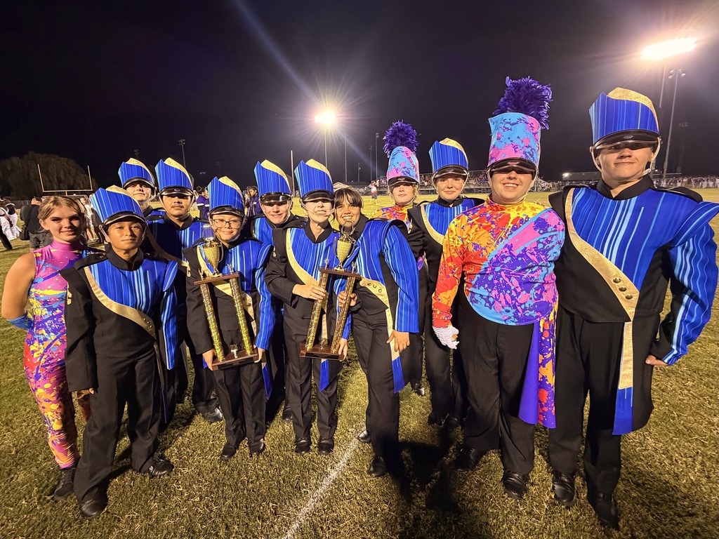 The band students are posed for a picture on the football field while holding the trophies that they won. 
