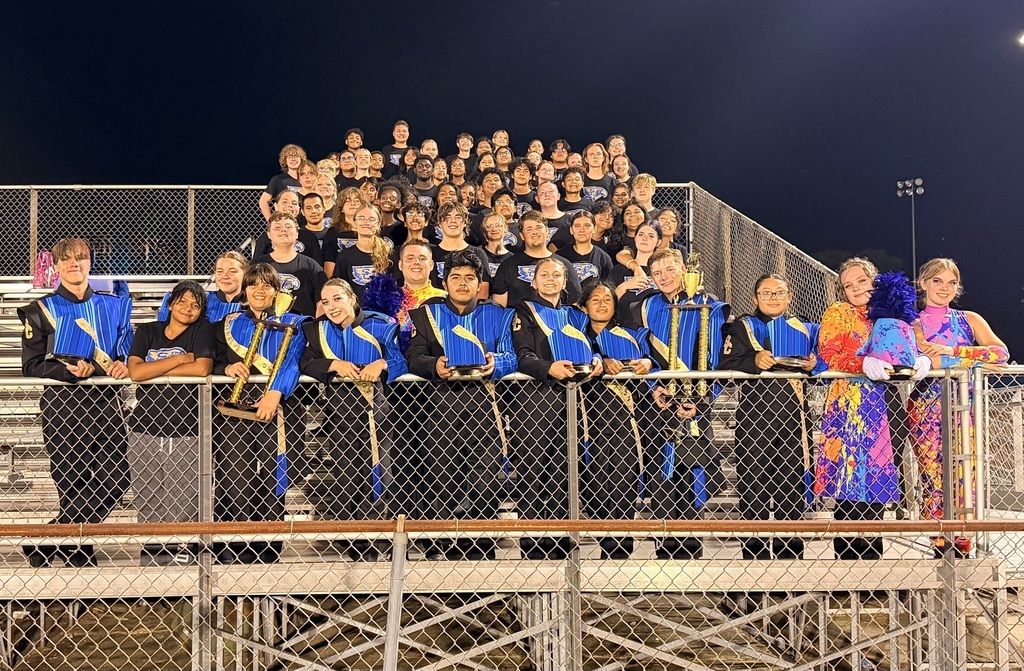 The band students are posed for a picture outside on the bleachers. 