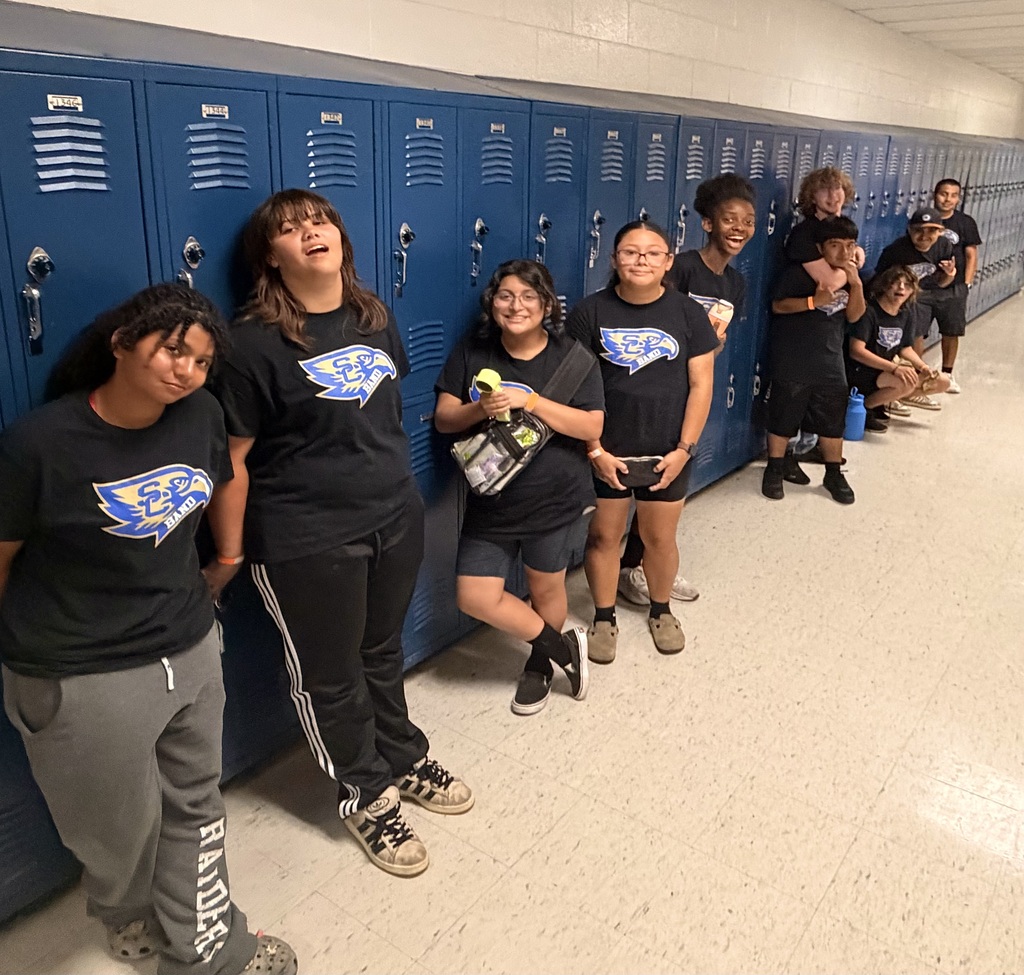 Some of the band students are standing in the hallway against their lockers. 