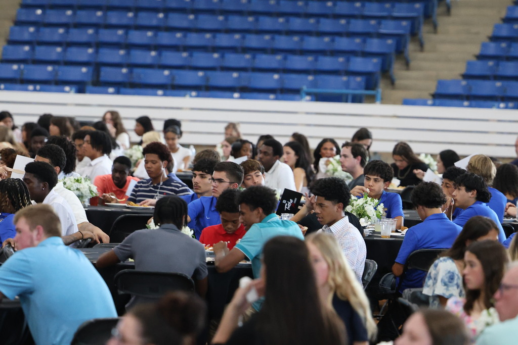 There are several tables in this picture with students all sitting at them. 