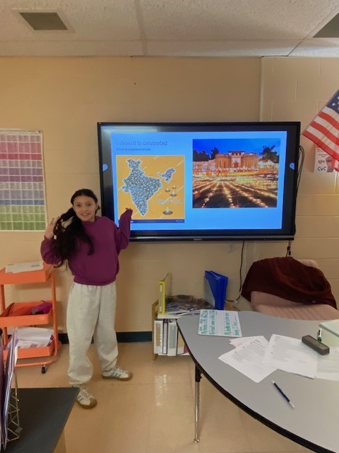 A student is standing in the classroom beside a touchscreen tv ready to give her presentation to the class. 