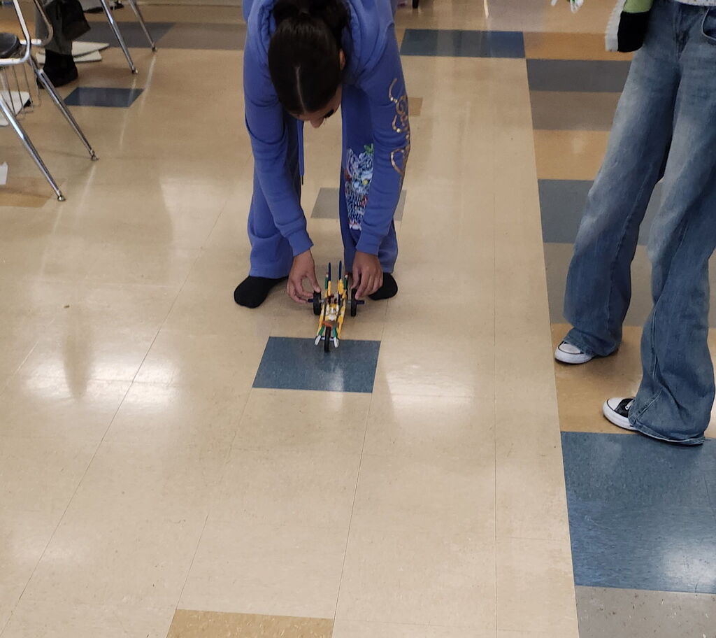 A student is trying out their K'nex car they built on the floor.