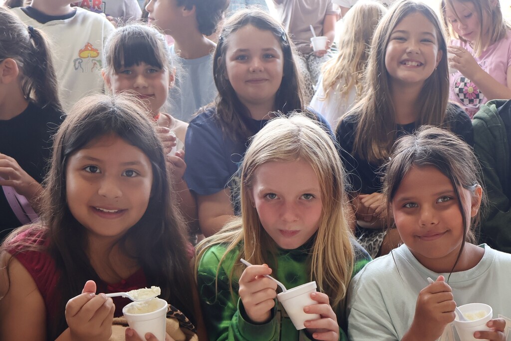 There are several students who are sitting on bleachers and each are eating a cup of ice cream. 