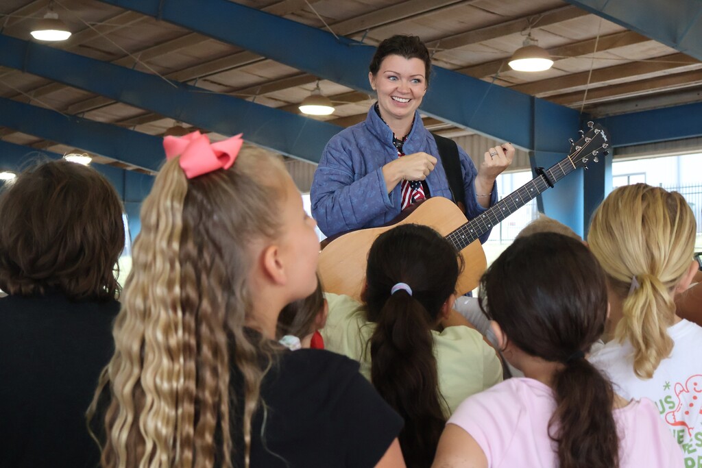 A woman is holding a guitar and talking to students. 