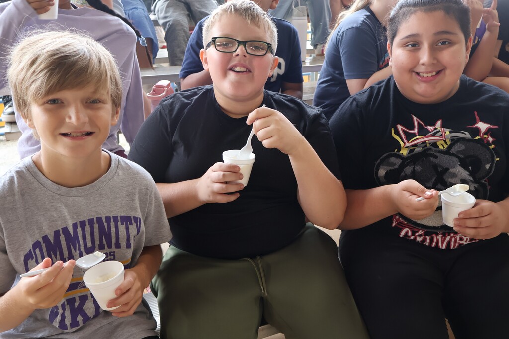 Three students are posing for a group picture while eating ice cream. 