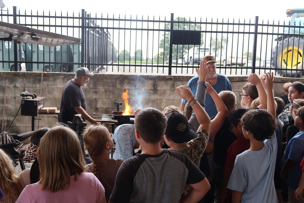 Students are watching a man make horse shoes. 