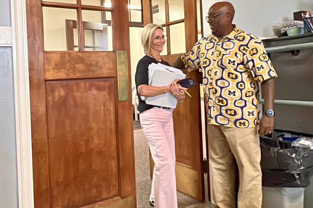 A woman is walking through door while a man is holding it open. 