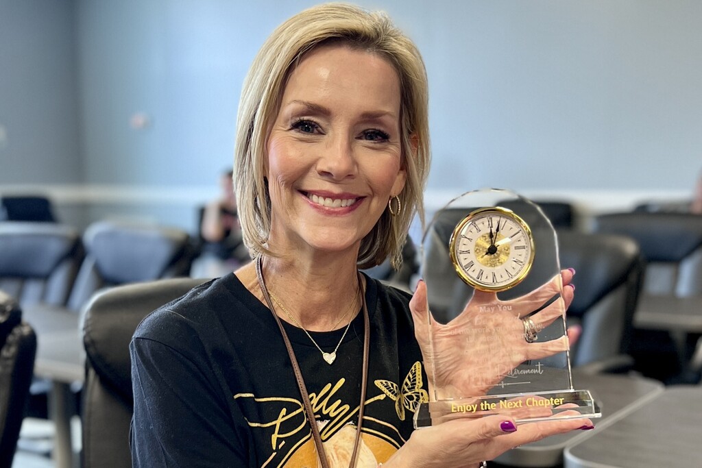 A woman is holding up a glass clock that she received as a gift. 