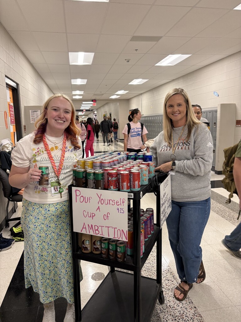  Ms. Wilson and Mrs. Demonbreum standing beside "Cup of Ambition" cart stocked with beverages in school hallway during 9-25 Dolly Day celebration. 