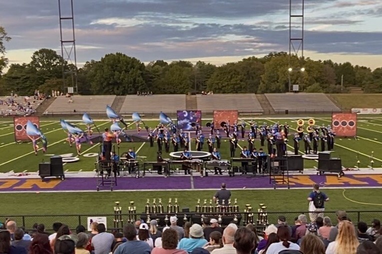 The marching band is on the football field during their performance. 