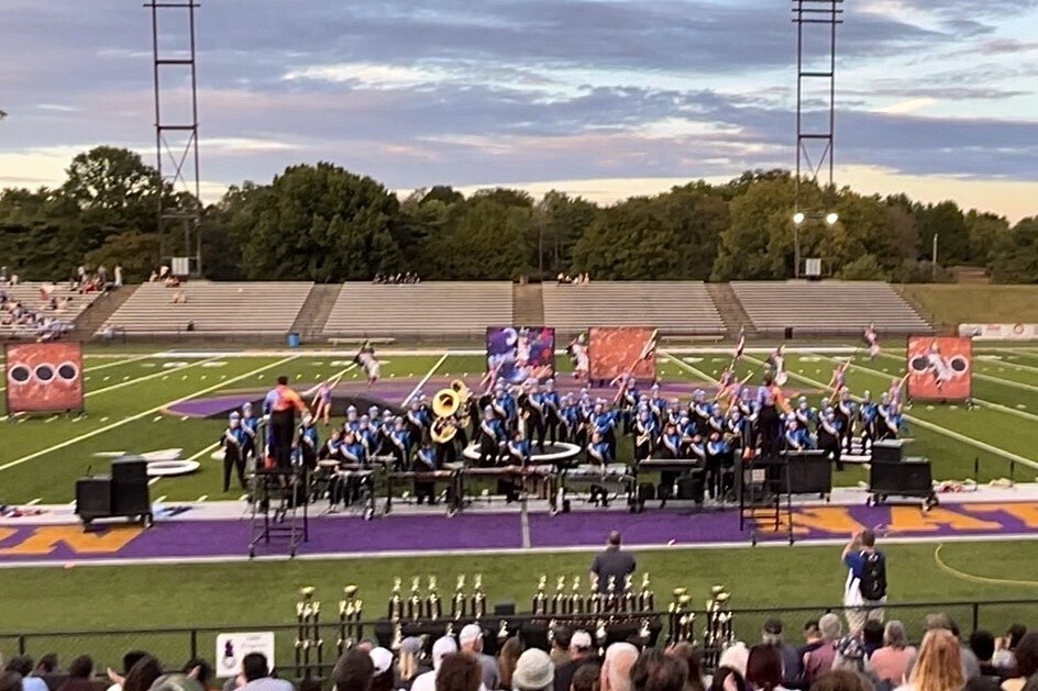 The marching band is on the football field during their performance. 