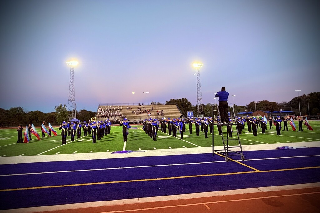 The marching band is on the football field during their performance. 
