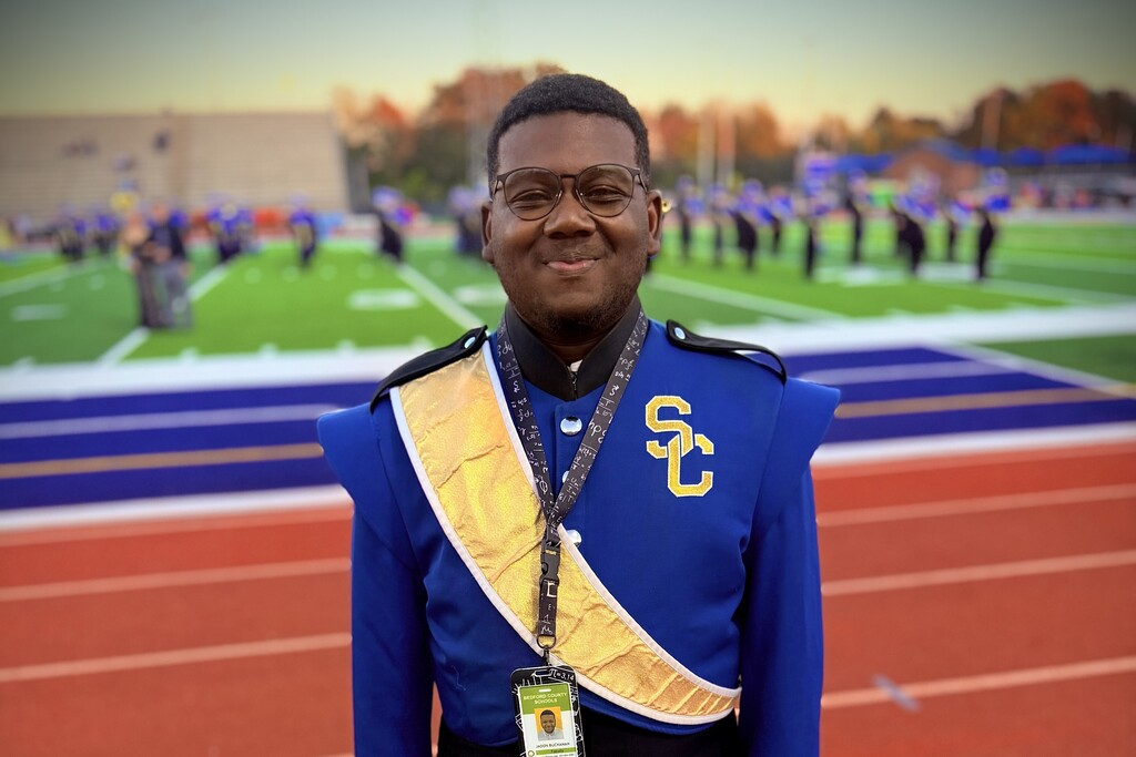 A marching band member poses for a picture while standing on the track. 