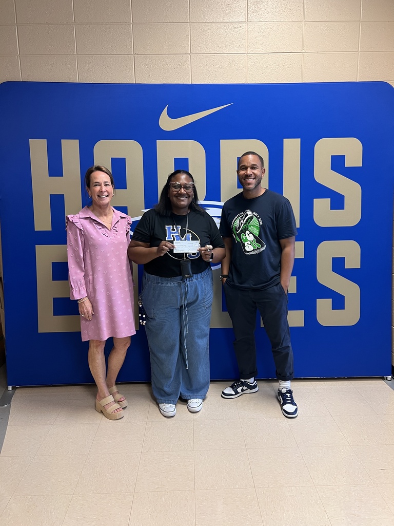 A man and two women are posed for a group picture in front of a backdrop that has "Harris Eagles" on it. 