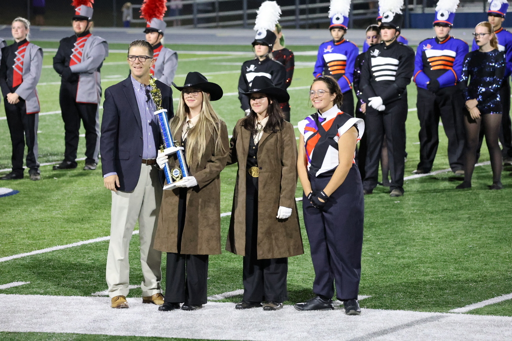 Three members of the marching band are posing for a picture on the football field holding the trophy their team was presented. 