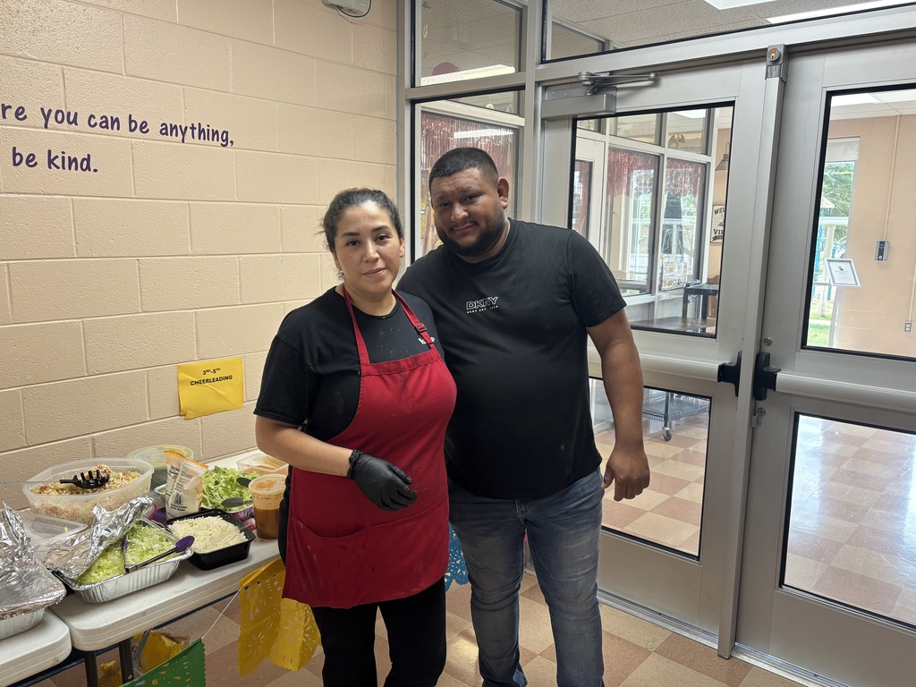 A woman and a man pose for a picture together in front of a table of food. 