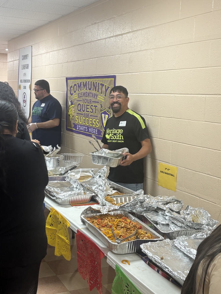 A man is standing behind a table that has food on it while serving it to other people. 