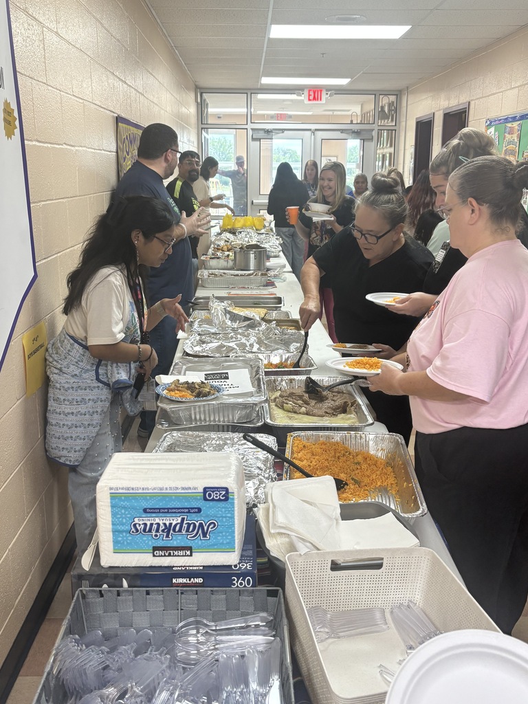 There are several people behind a table that has food on it while others are in front of them getting plates of food. 