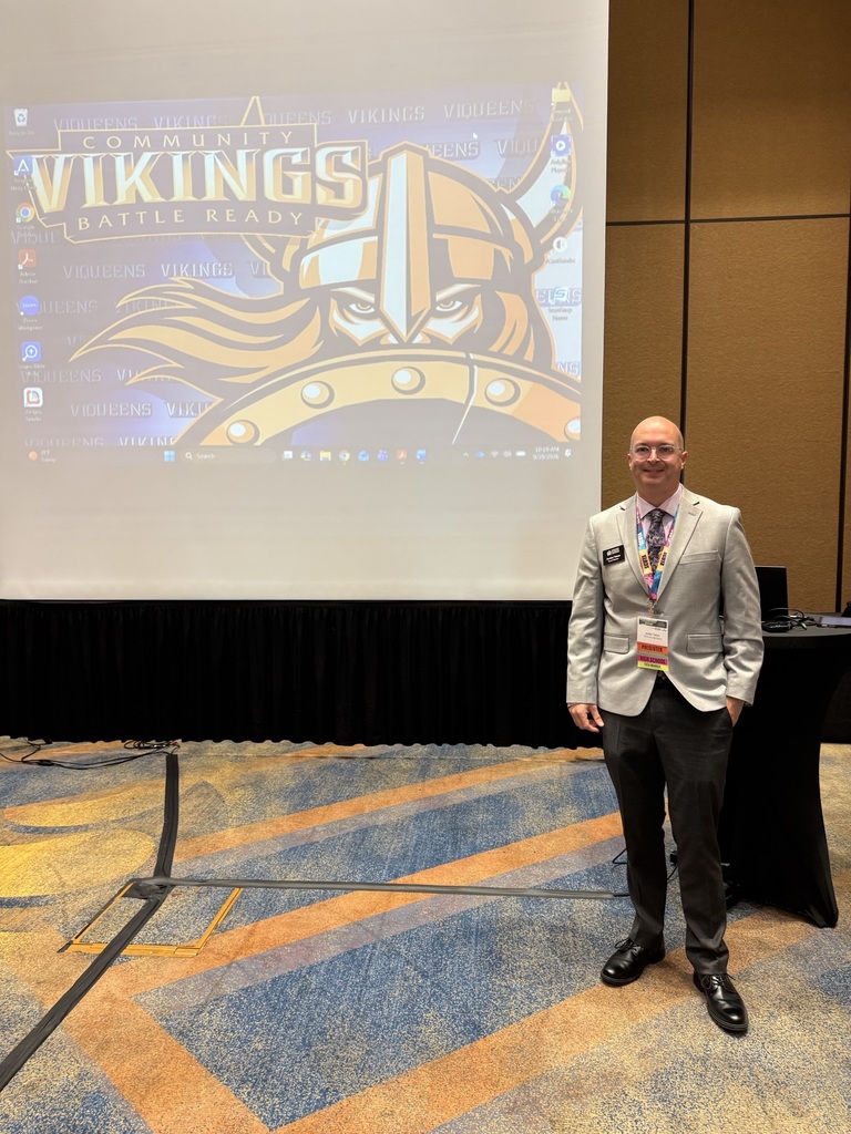 A man is posed in front of a large backdrop with the Community Vikings Battle Ready logo on the screen.