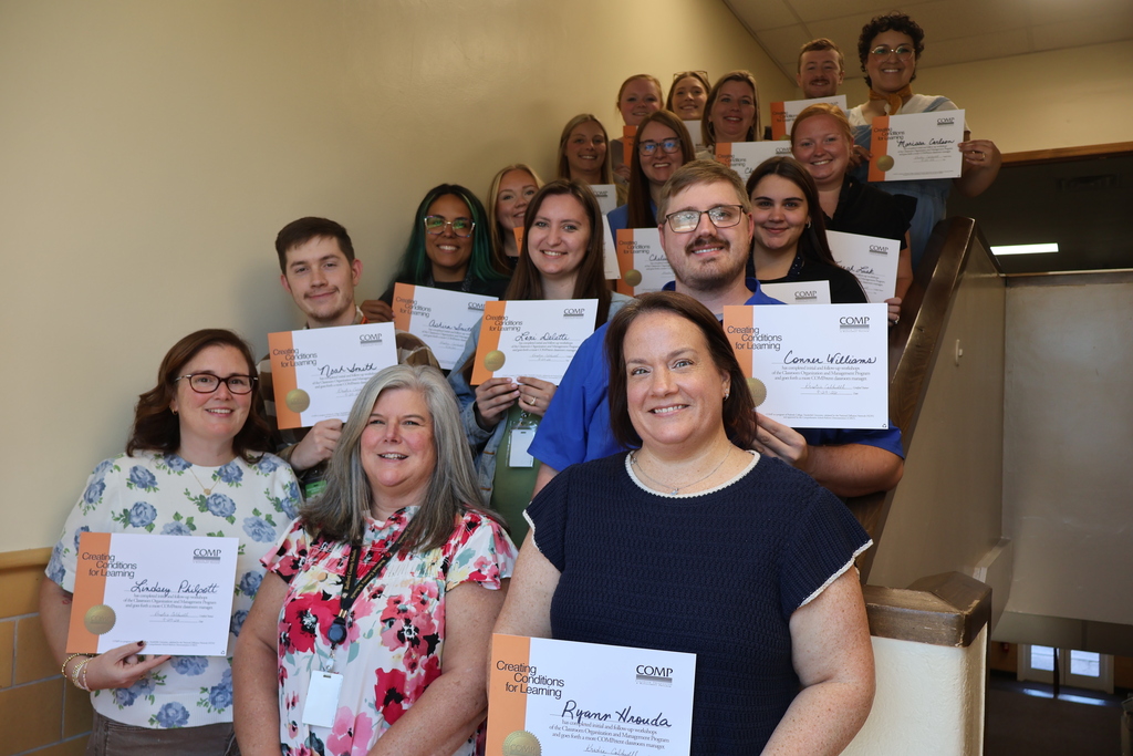 A group of people are all gathered for a group picture and all but one person is holding up their certificate. 