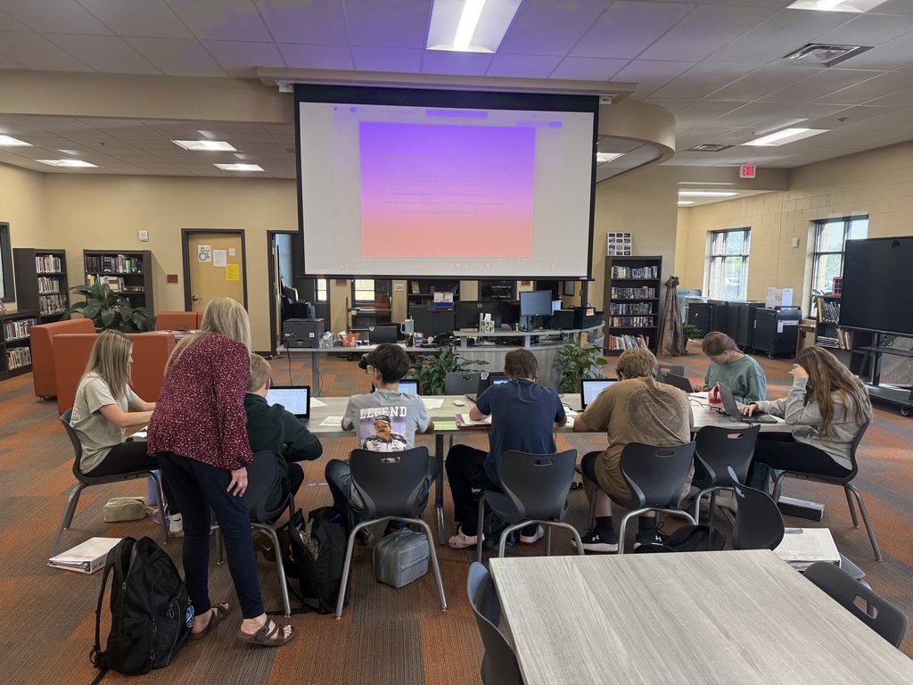  Mr. Simmons's 5th period World History students working on laptops in library learning to create MLA Works Cited page with librarian Mrs. Thomas, projection screen displaying Works Cited document.