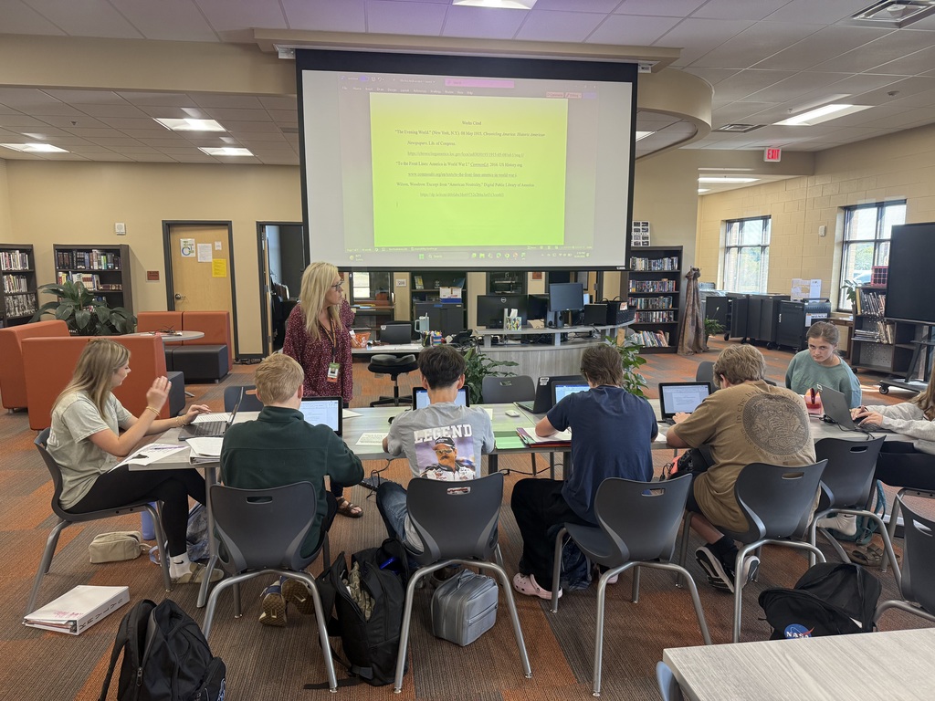  Mr. Simmons's 5th period World History students working on laptops in library learning to create MLA Works Cited page with librarian Mrs. Thomas, projection screen displaying Works Cited document.