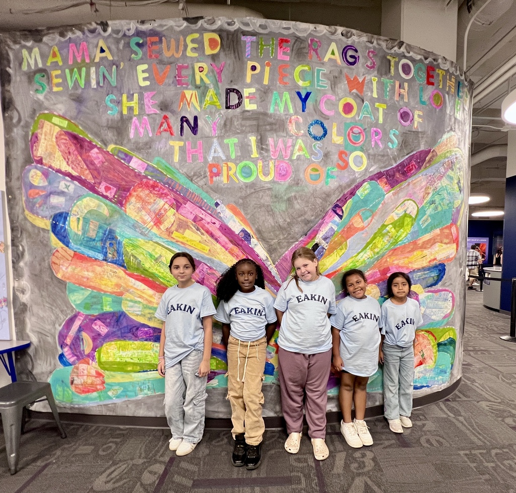 There are five girls all posed in front of a colorful wall that has a butterfly painted on it.