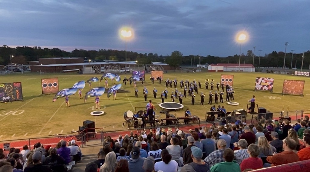 The marching band is on the football field during their performance.