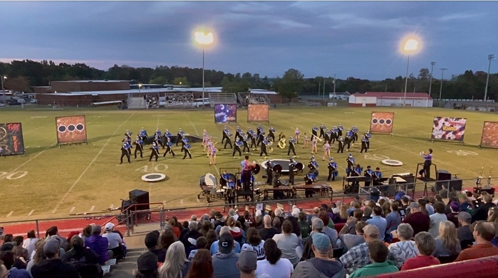The marching band is on the football field during their performance.