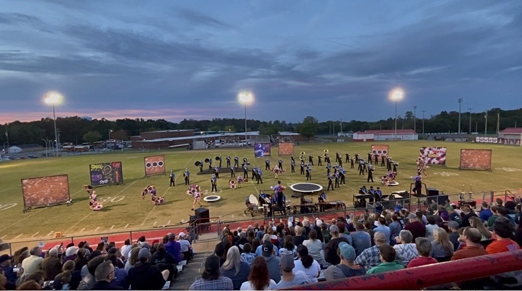 The marching band is on the football field during their performance.