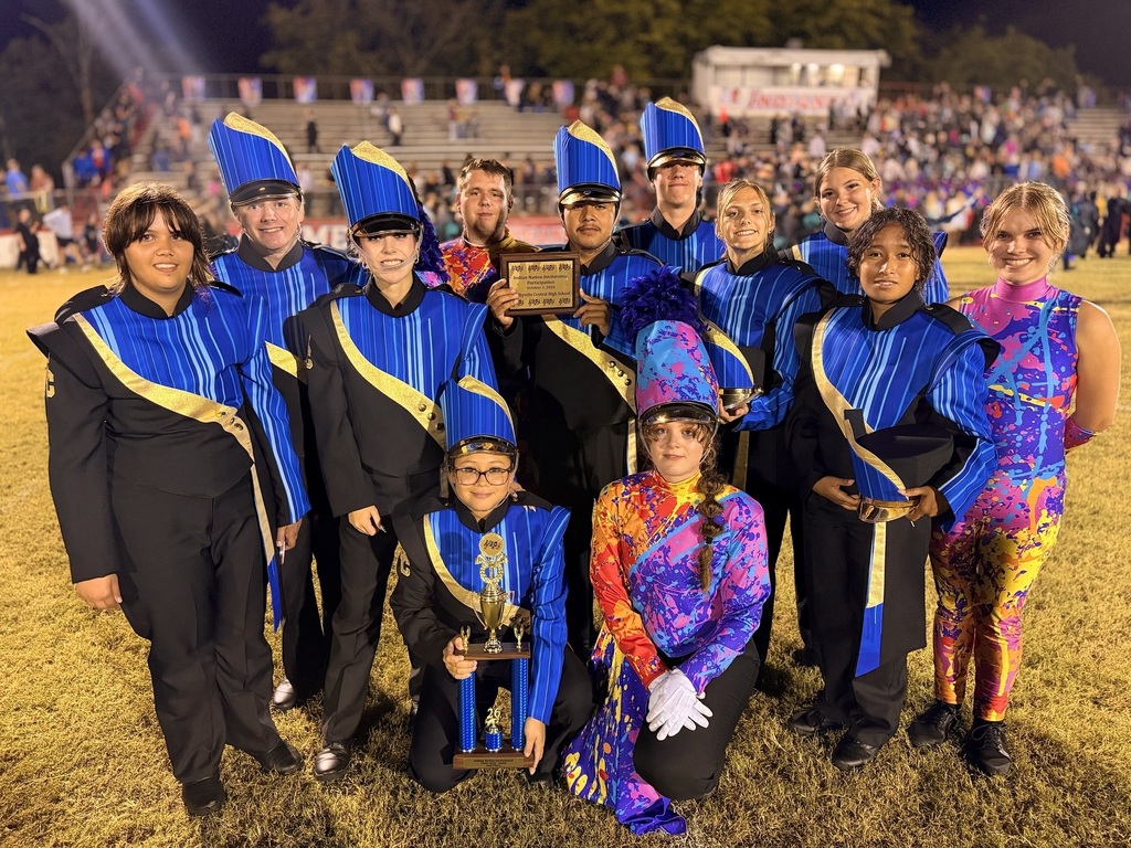 Several band members are posed for a picture on the football field holding a trophy and plaque that they received for their performance.