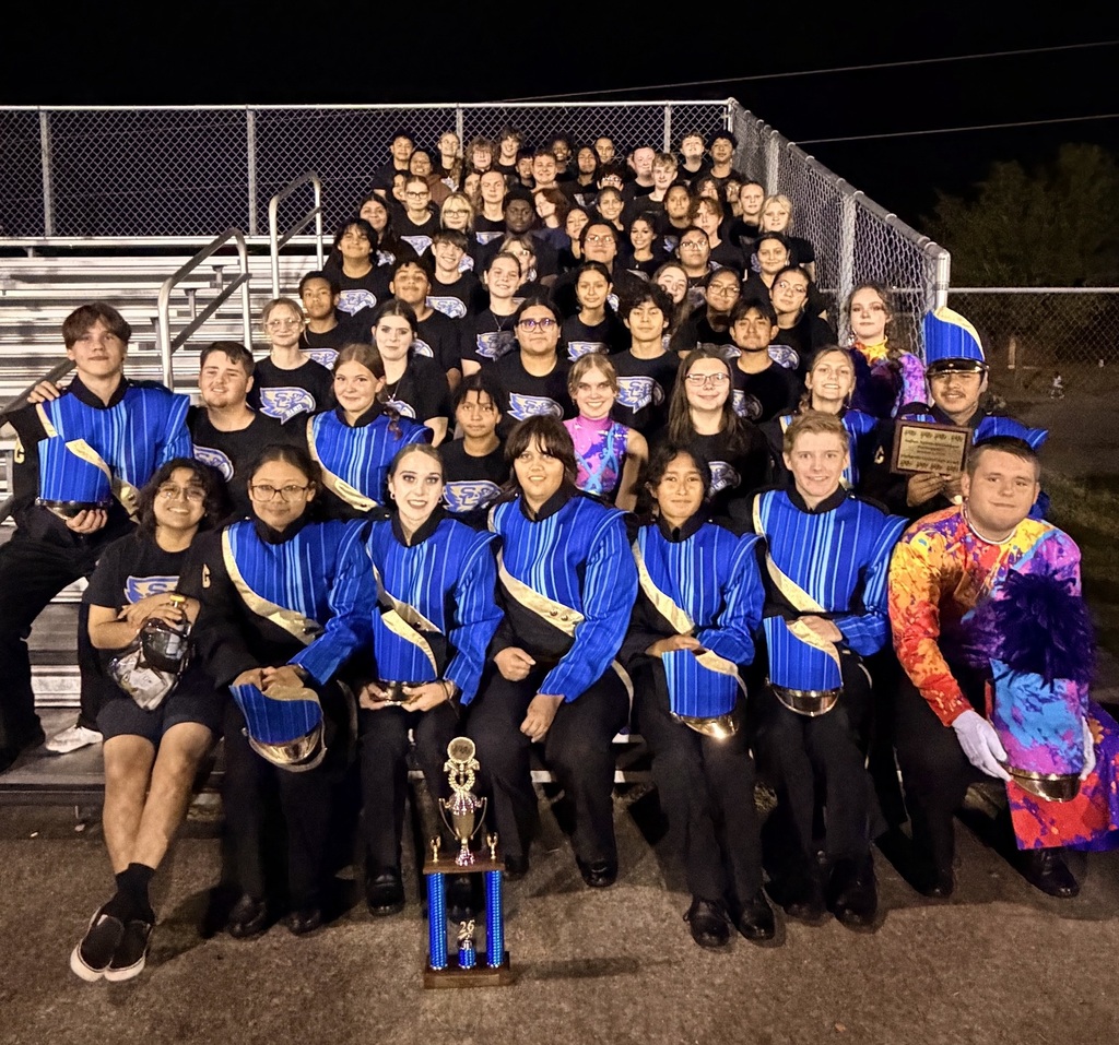 Members of the marching band are posed for a picture on the bleachers at the football field.