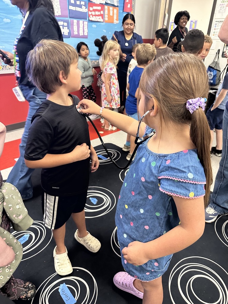 A first grader is listening to her fellow classmate's heartbeat.