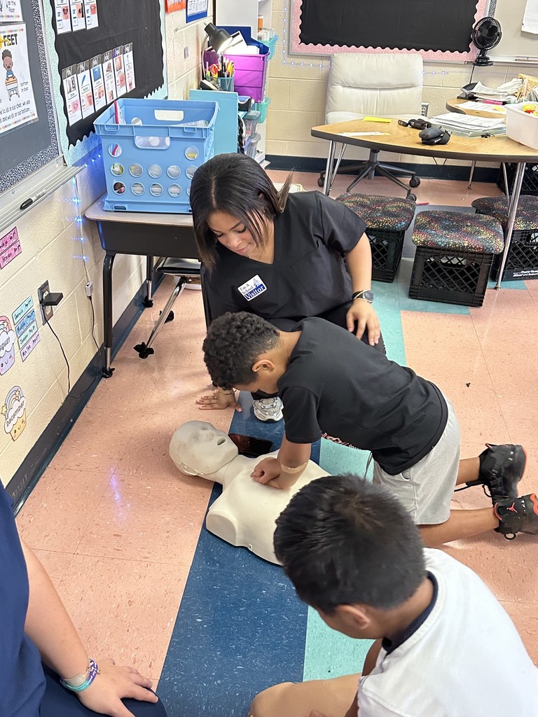 A HOSA student is showing a younger student how to give CPR on a mannequin.