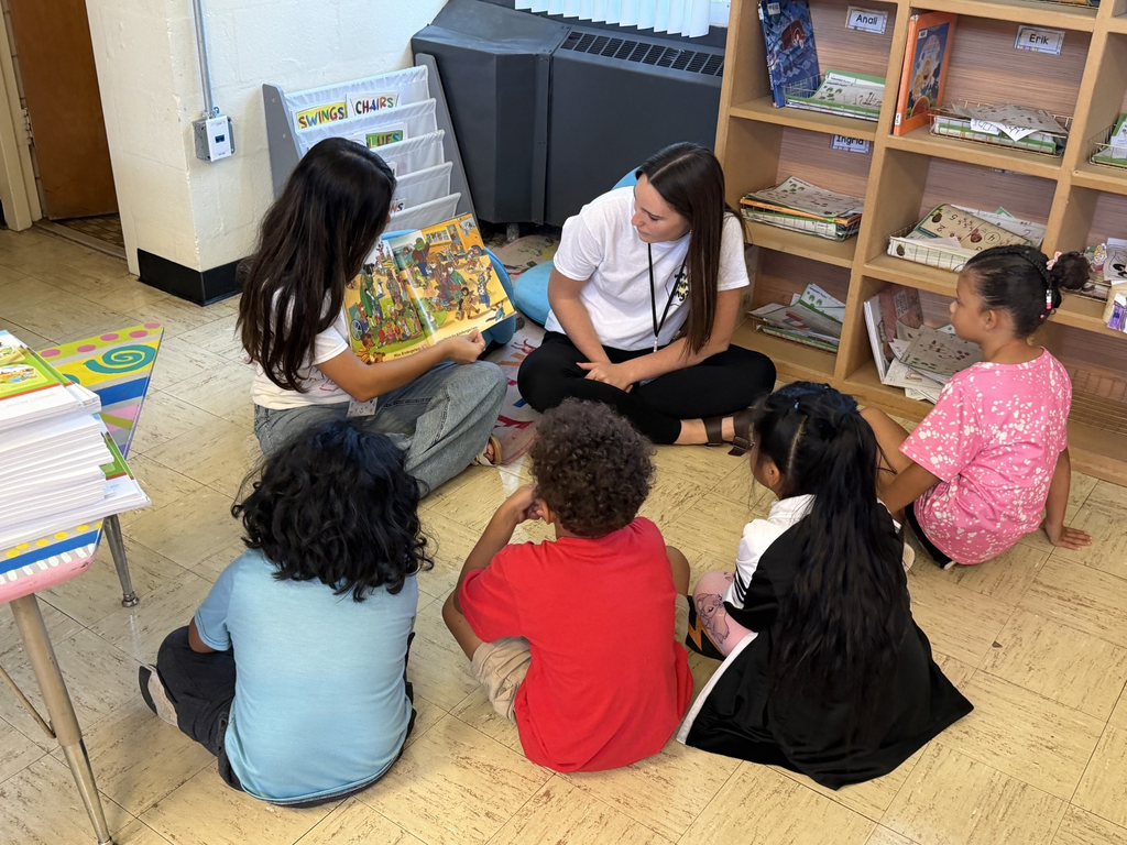 Two high school students are sitting on the floor reading a book to four kindergarten students.