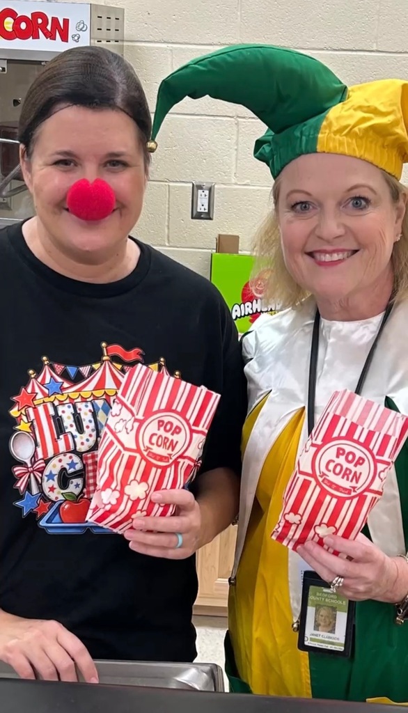 Two women are dressed up in circus themed clothes and each are holding a bag of popcorn. 