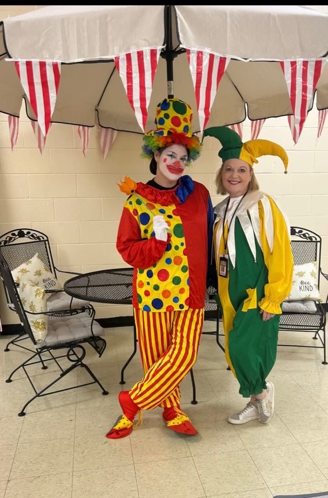 Two women dressed as clowns pose for a group picture in the cafeteria. 