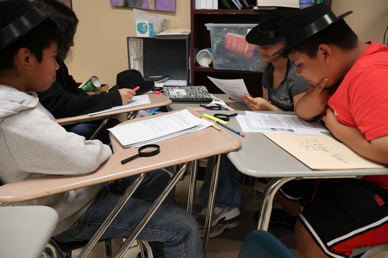 Four students are sitting at their desks discussing the book and their findings.