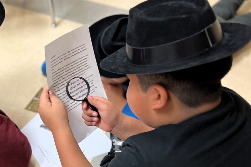 A student is using a magnifying glass to read a piece of paper.