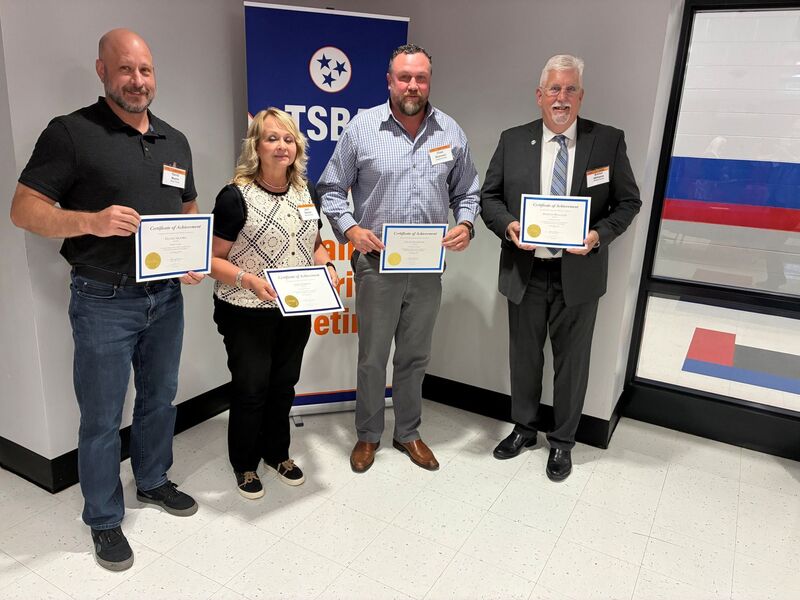 There are four people all posed for a group picture while holding up certificates.