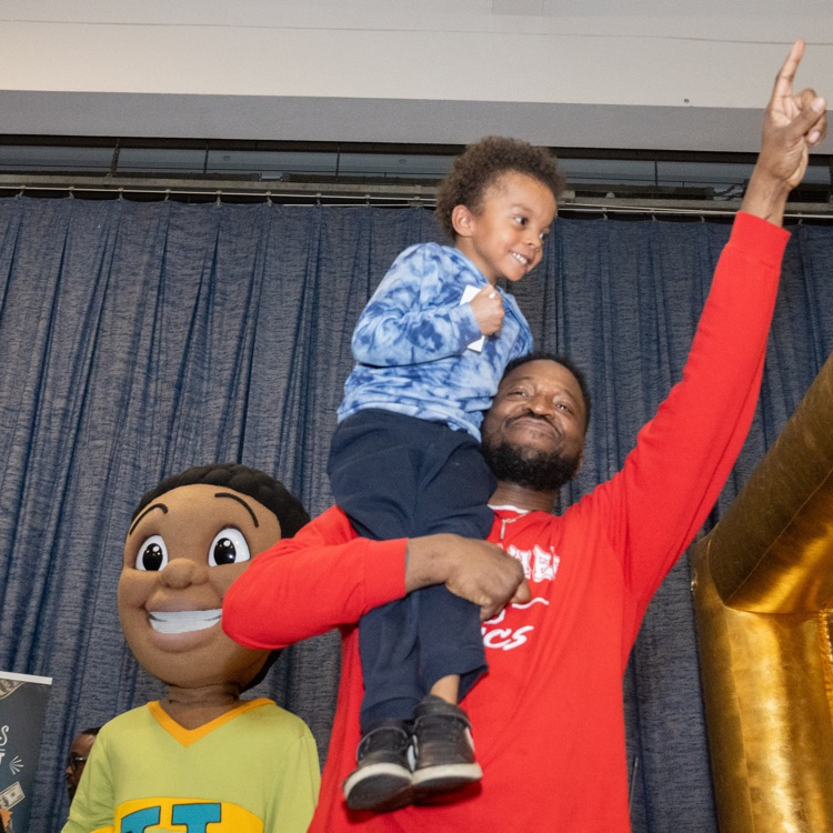 Parent holding their student  posing next to the Character John John 